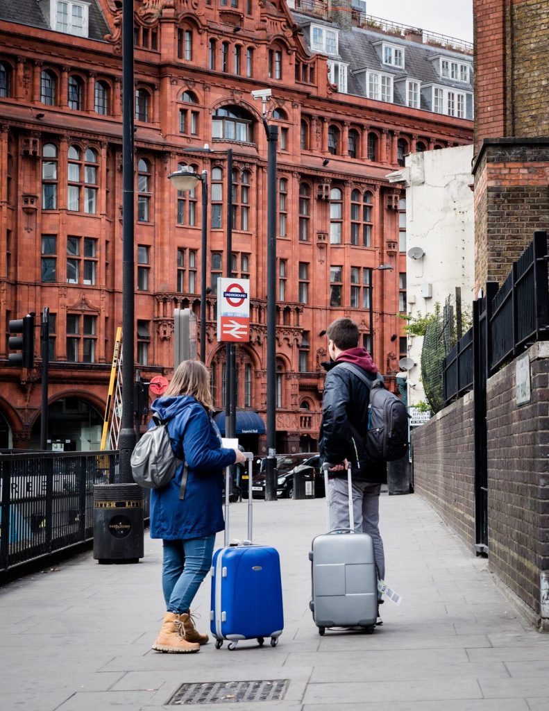 A couple with suitcases stands on a London sidewalk, showcasing urban travel and architecture.