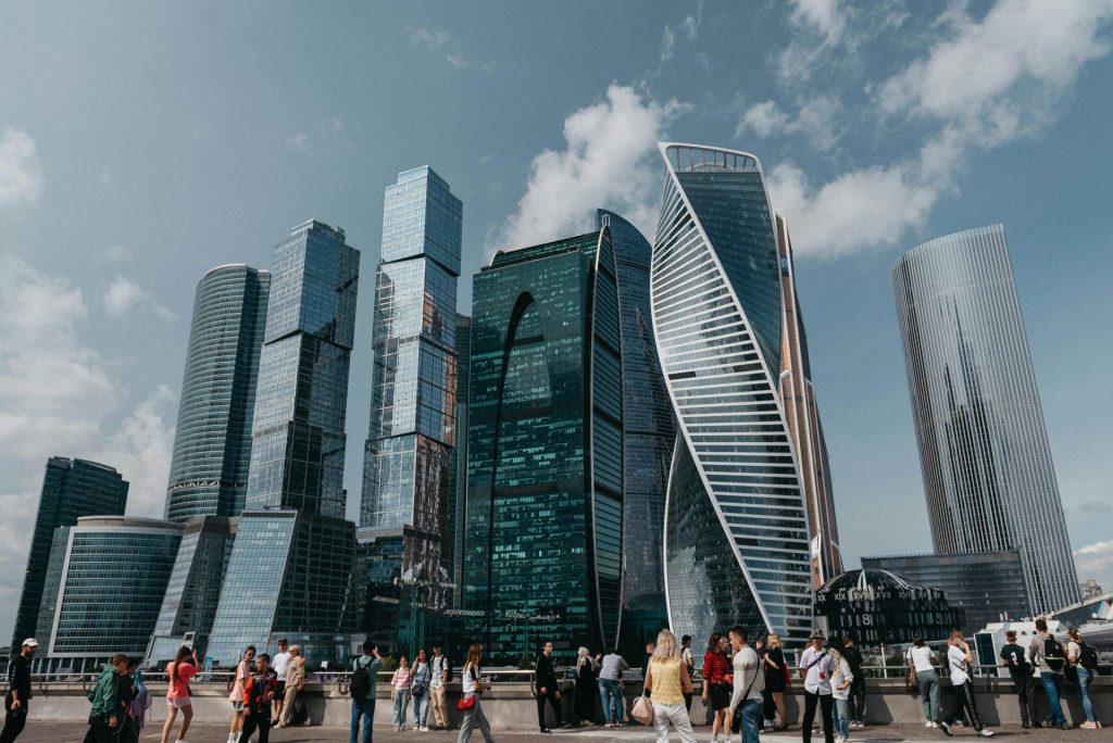 Diverse crowd stands in front of iconic modern skyscrapers in a vibrant cityscape.