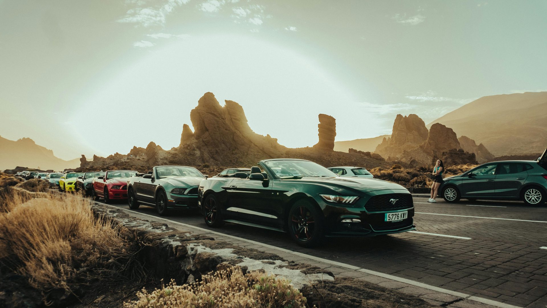 Cars lined up on a scenic road with striking rock formations during sunset.