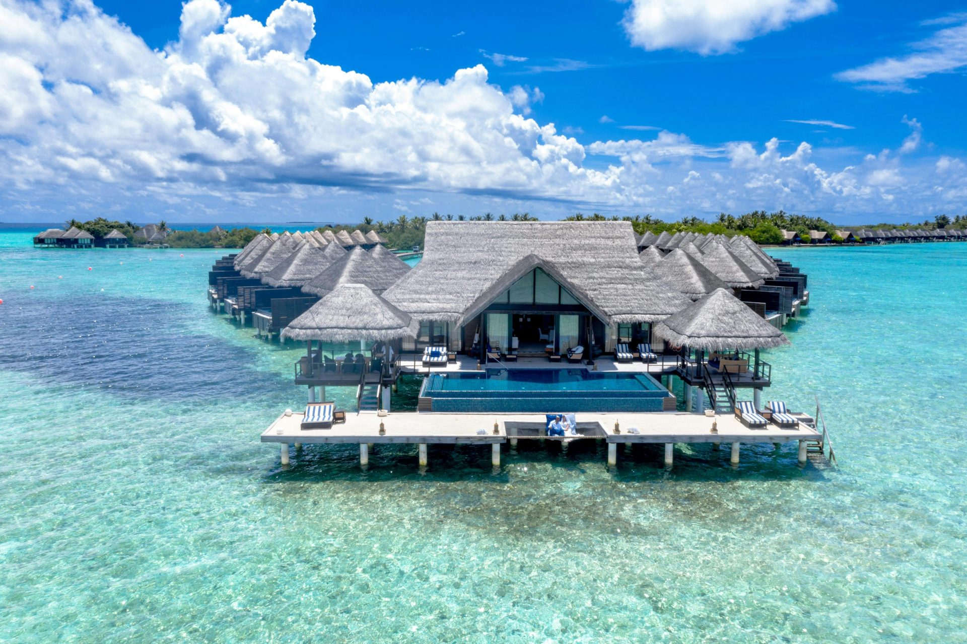 Aerial view of luxurious overwater bungalows with thatched roofs over turquoise waters in a tropical paradise.
