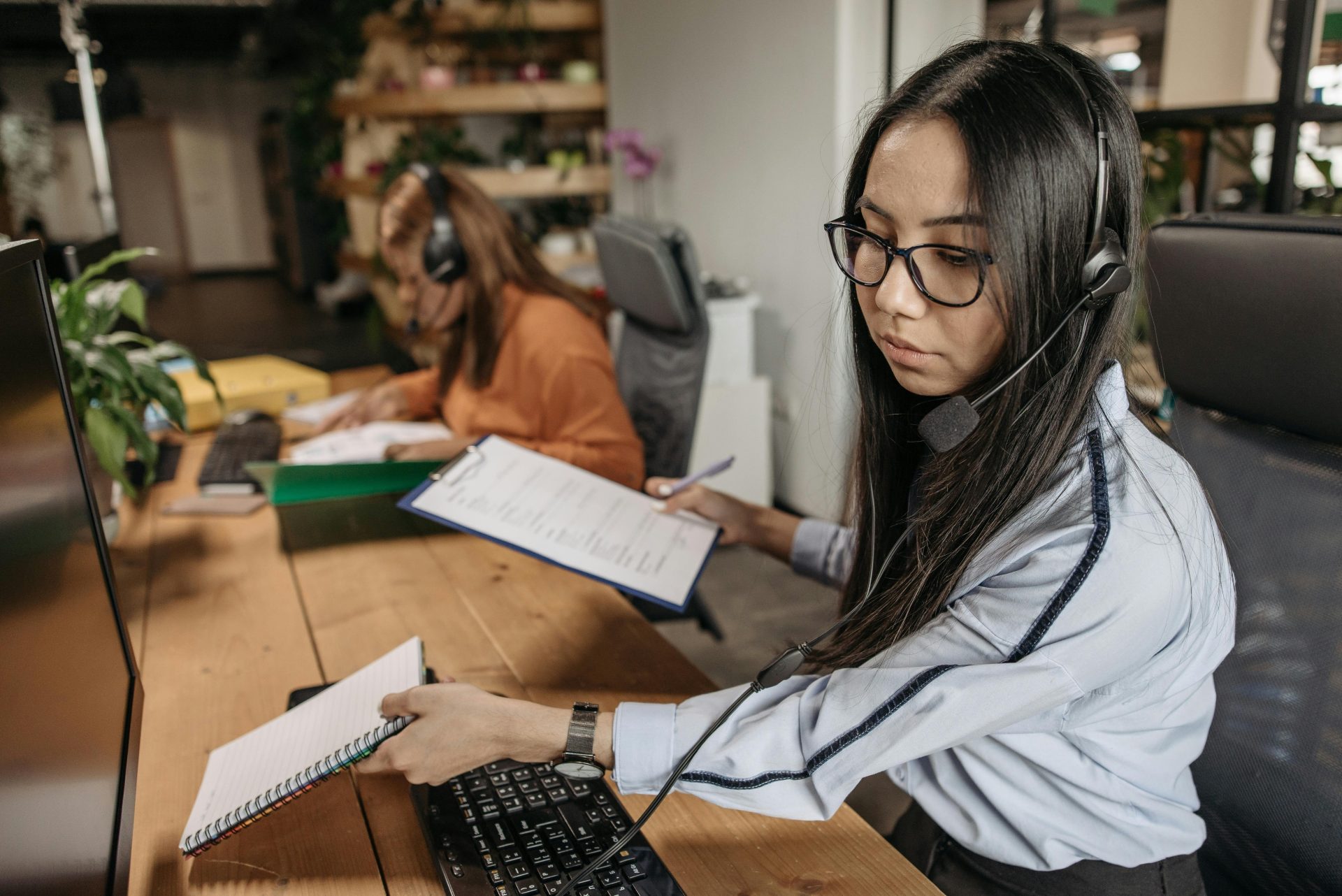 Focused call center agent wearing headset, managing paperwork at office desk.